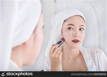 woman looking in the mirror and applying cosmetic with a brush