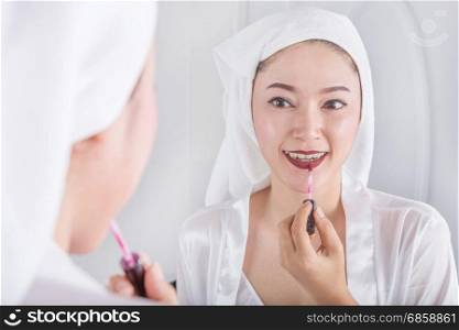 woman looking in the mirror and applying red lipstick on her lips