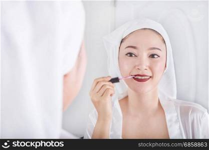 woman looking in the mirror and applying red lipstick on her lips