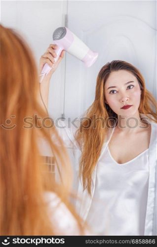 woman looking in the mirror drying her hair in bathroom