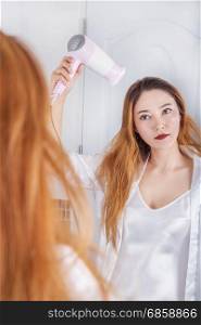 woman looking in the mirror drying her hair in bathroom