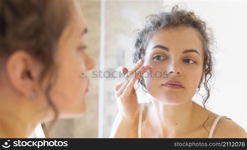 woman looking mirror applying cream face