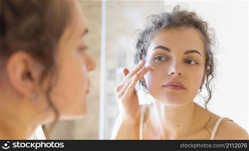 woman looking mirror applying cream face