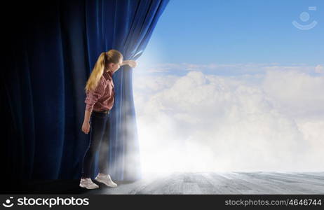 Woman looking out from curtain. Young woman in casual opening blue curtain and looking at clear sky