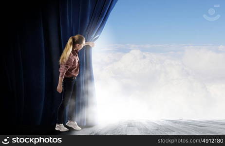 Woman looking out from curtain. Young woman in casual opening blue curtain and looking at clear sky