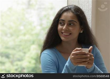 woman looking outside window while sipping coffee