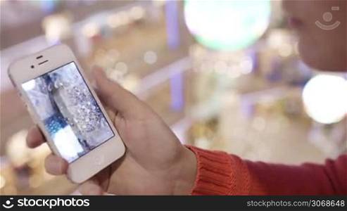 Woman looking through the photos of Christmas tree in her smartphone with zooming of one of them.
