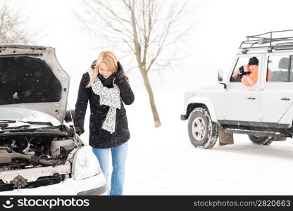 Woman looking under broken car hood snow trouble man assistance