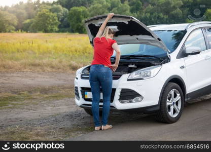 Woman looking under the hood of broken car at offroad