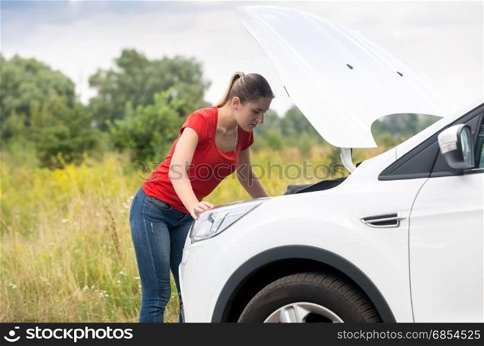 Woman looking under the hood of overheated car at meadow
