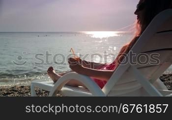 woman looks at the sunset while sitting on the beach with a cocktail