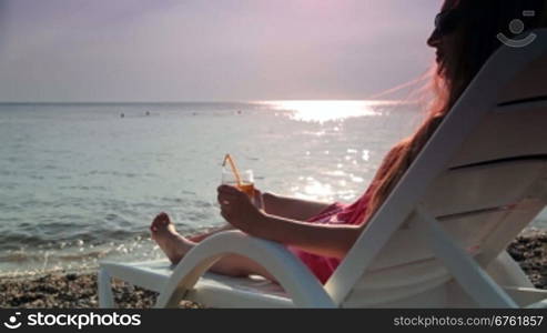 woman looks at the sunset while sitting on the beach with a cocktail