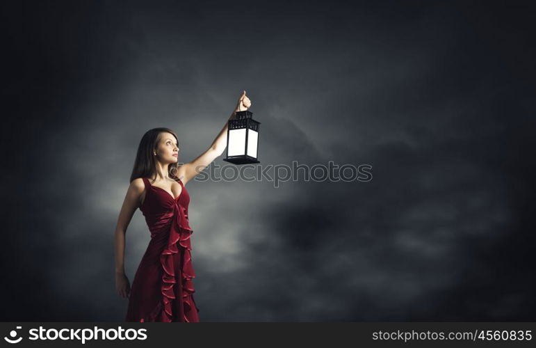 Woman lost in darkness. Young attractive woman in red dress with lantern