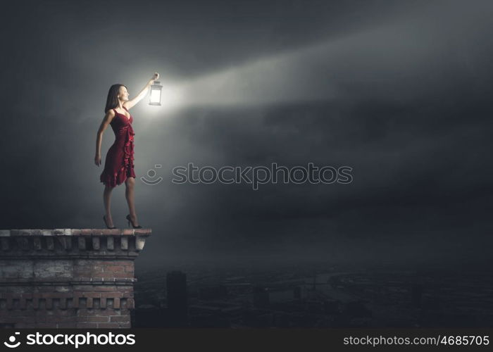 Woman lost in darkness. Young attractive woman in red dress with lantern