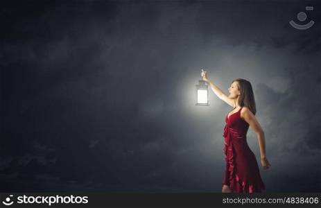 Woman lost in darkness. Young attractive woman in red dress with lantern