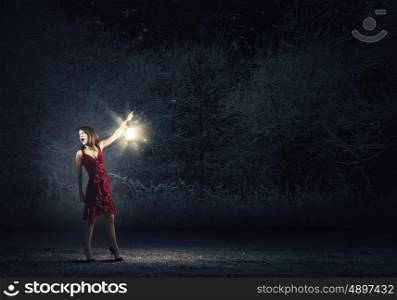 Woman lost in darkness. Young attractive woman in red dress with lantern