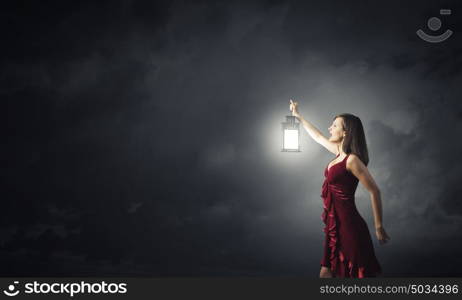 Woman lost in darkness. Young attractive woman in red dress with lantern