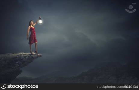 Woman lost in darkness. Young attractive woman in red dress with lantern