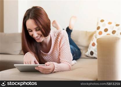Woman lying down on couch with a tablet