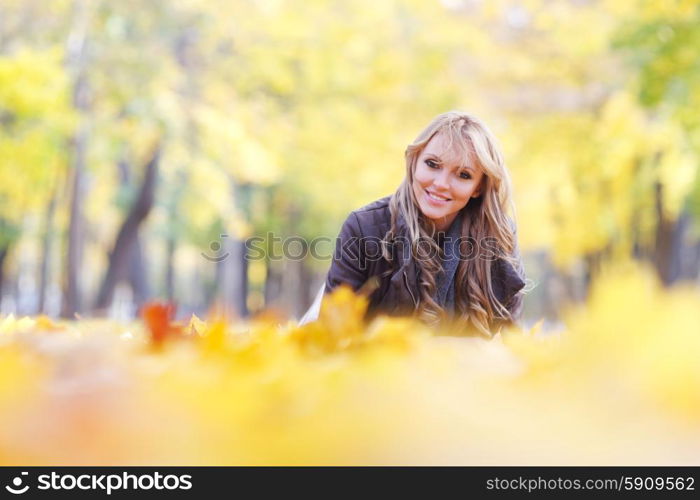 Woman lying in autumn leaves . Portrait of a cute smiling woman lying in autumn leaves in park