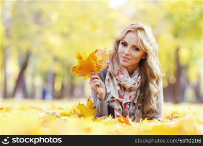Woman lying in autumn leaves . Portrait of a cute smiling woman lying in autumn leaves in park
