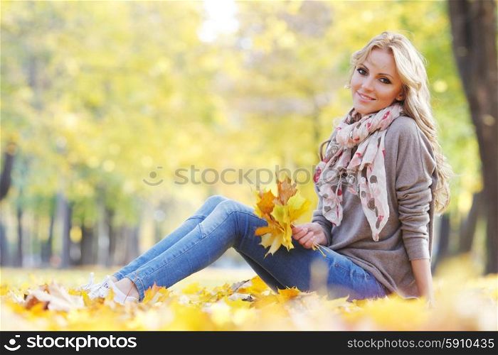 Woman lying in autumn leaves . Portrait of a cute smiling woman sitting on autumn leaves in park