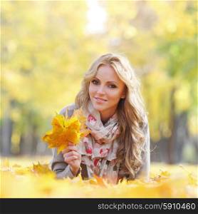 Woman lying in autumn leaves . Portrait of a cute smiling woman lying in autumn leaves in park
