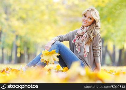 Woman lying in autumn leaves . Portrait of a cute smiling woman sitting on autumn leaves in park