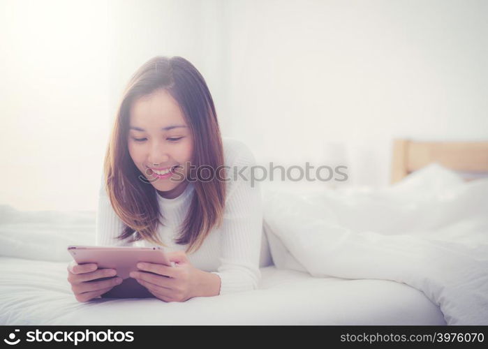 woman lying in bedroom with digital tablet touching with finger in morning sunlight