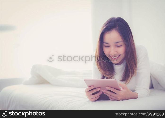 woman lying in bedroom with digital tablet touching with finger in morning sunlight