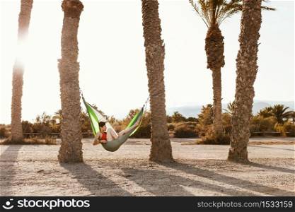 Woman lying in hammock between palm trees on the beach