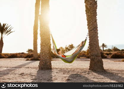 Woman lying in hammock between palm trees on the beach