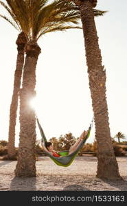 Woman lying in hammock between palm trees on the beach