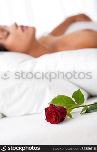 Woman lying in white bed, focus on rose, shallow DOF