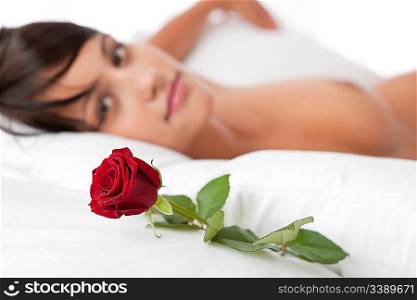 Woman lying in white bed, focus on rose, shallow DOF