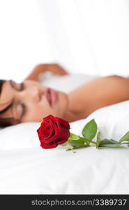 Woman lying in white bed, focus on rose, shallow DOF
