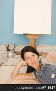 Woman lying infront on an easel and paintbrushes
