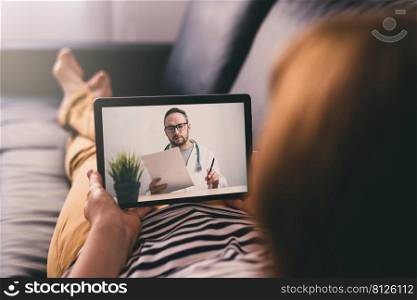 Woman lying on a sofa at home and talking with a doctor online using digital tablet. Telemedicine concept.. Woman lying on a sofa and talking with a doctor online using digital tablet. Telemedicine concept.