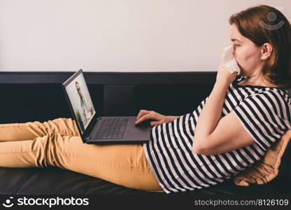 Woman lying on a sofa at home and talking with a doctor online using laptop. Telemedicine concept.. Woman lying on a sofa and talking with a doctor online using laptop. Telemedicine concept.