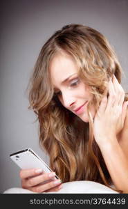 Woman lying on bed with phone gray background