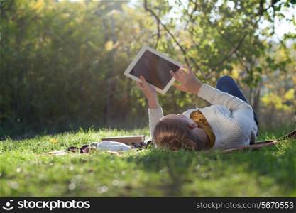 woman lying on bedding on green grass with ipad during picknic in the park