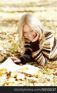 Woman lying on fallen leaves in autumn park and reading a book. Woman reading book