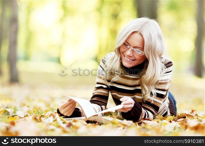 Woman lying on fallen leaves in autumn park and reading a book. Woman reading book