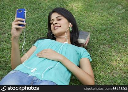 Woman lying on grass listening to mp3 player