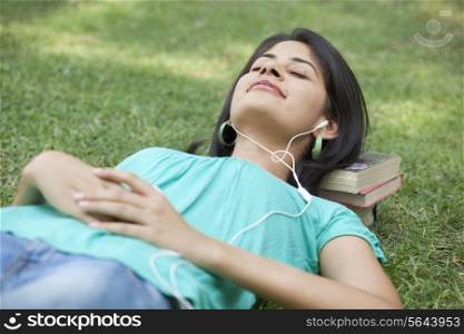 Woman lying on grass listening to music with eyes closed