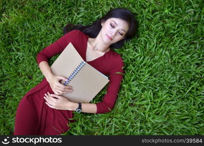 Woman lying on green grass with a book