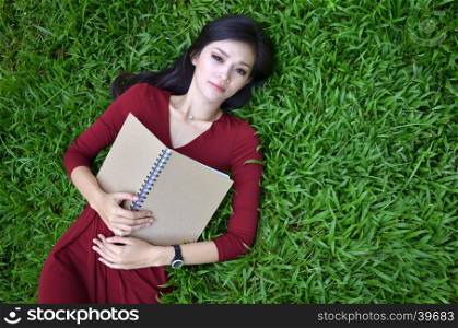 Woman lying on green grass with a book