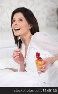 Woman lying on her bed with a glass of fruit salad