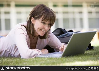 Woman lying on lawn of school with laptop