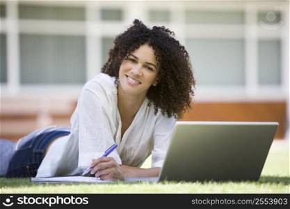 Woman lying on lawn of school with laptop